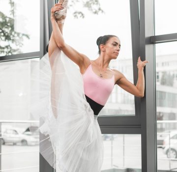 Erwachsenen-Ballettkurs – Tänzerin in rosa und weißem Tütü beim Stretching am Fenster